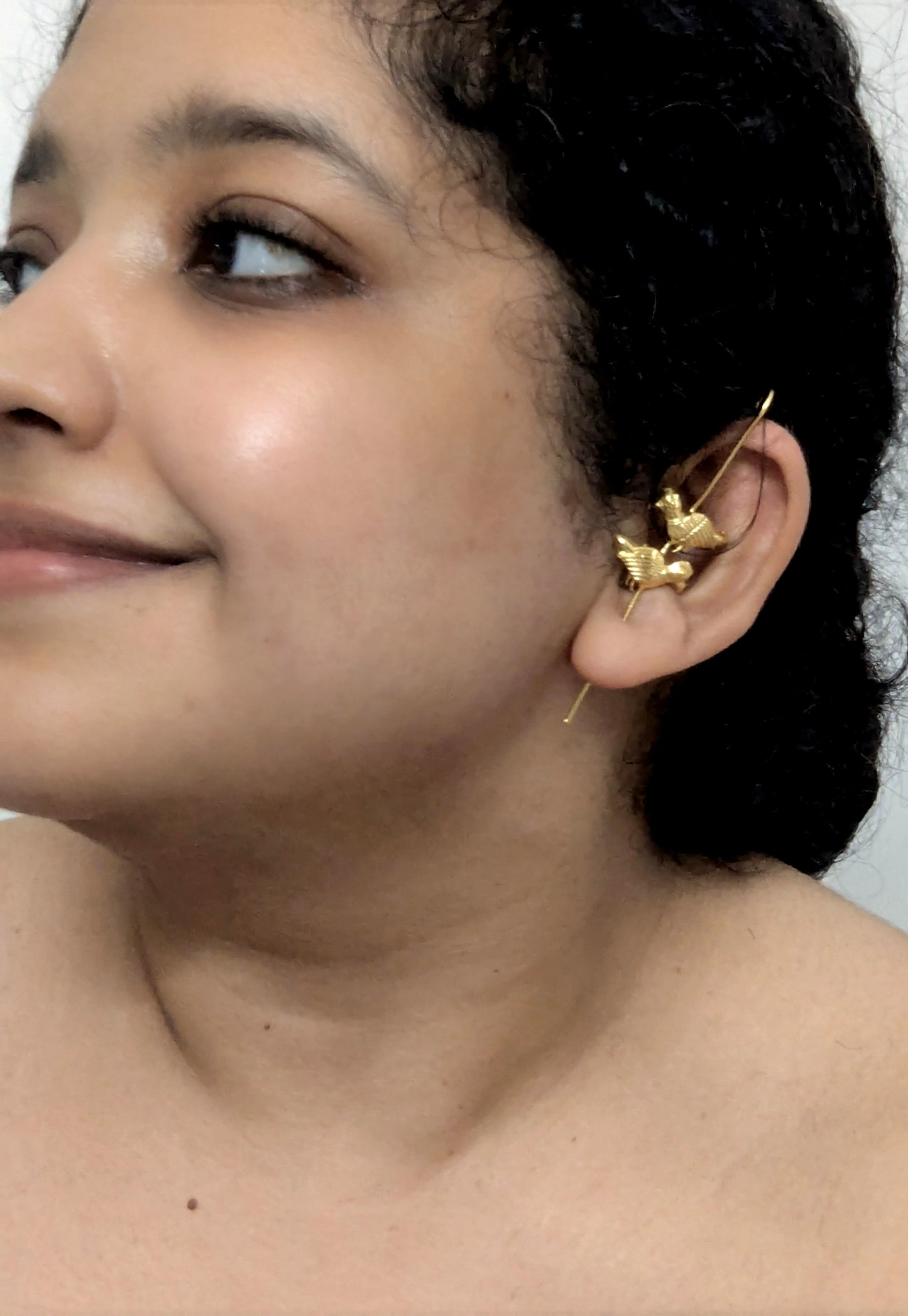 Close-up of a person wearing a gold earring with a neutral background