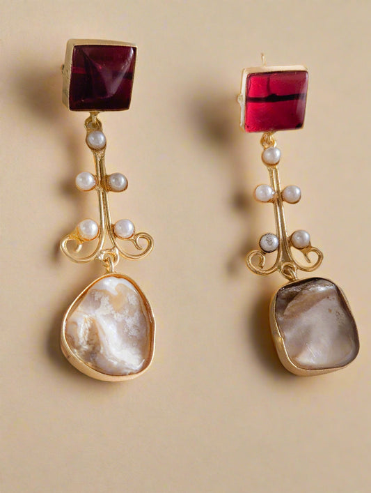 Pair of earrings with red gemstones, gold accents, and pearl-like beads on a beige background