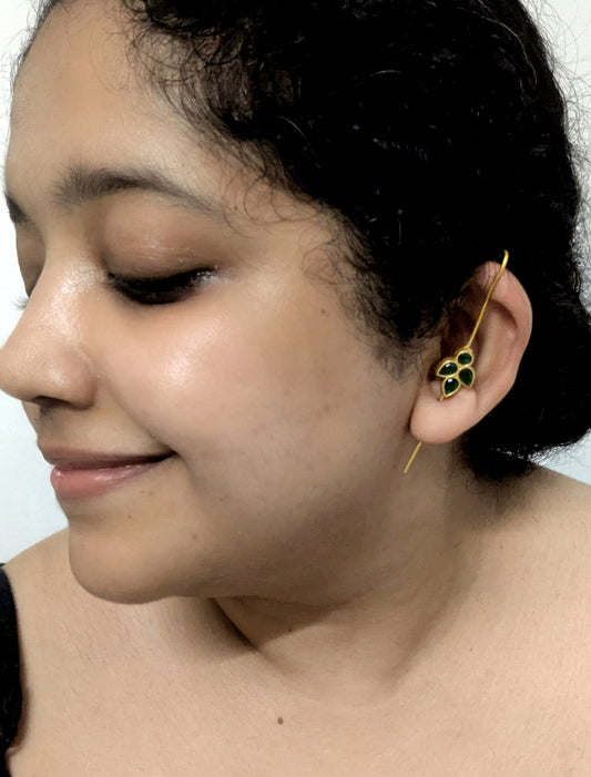 Close-up of a person wearing a gold earring with green stones on a plain background