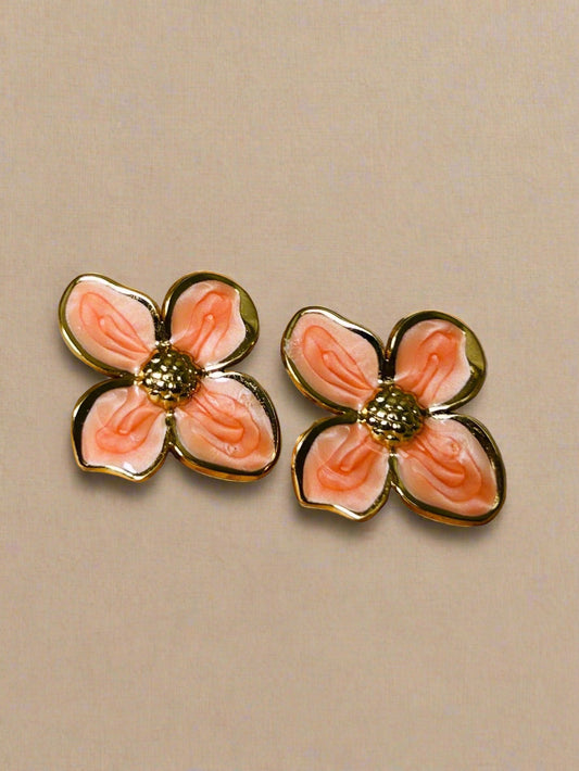 Pair of pink flower-shaped earrings with gold accents on a wooden surface.