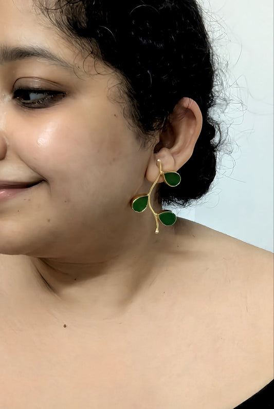 Woman wearing green leaf-shaped earrings against a plain background