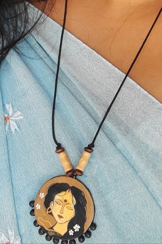 Necklace with a pendant featuring a face design, worn by a person in a light blue saree