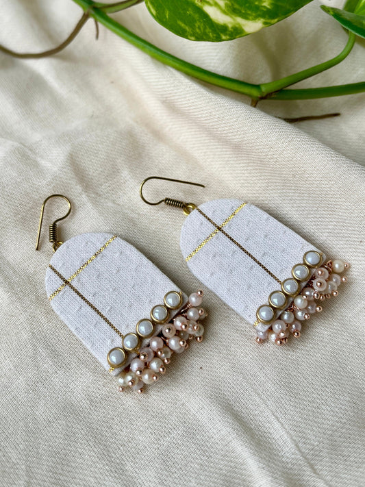 Pair of earrings with white fabric-like design and pearl embellishments on a beige background.