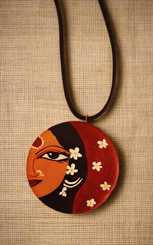 Necklace with a circular pendant featuring a stylized face and flowers on a brown textured background.